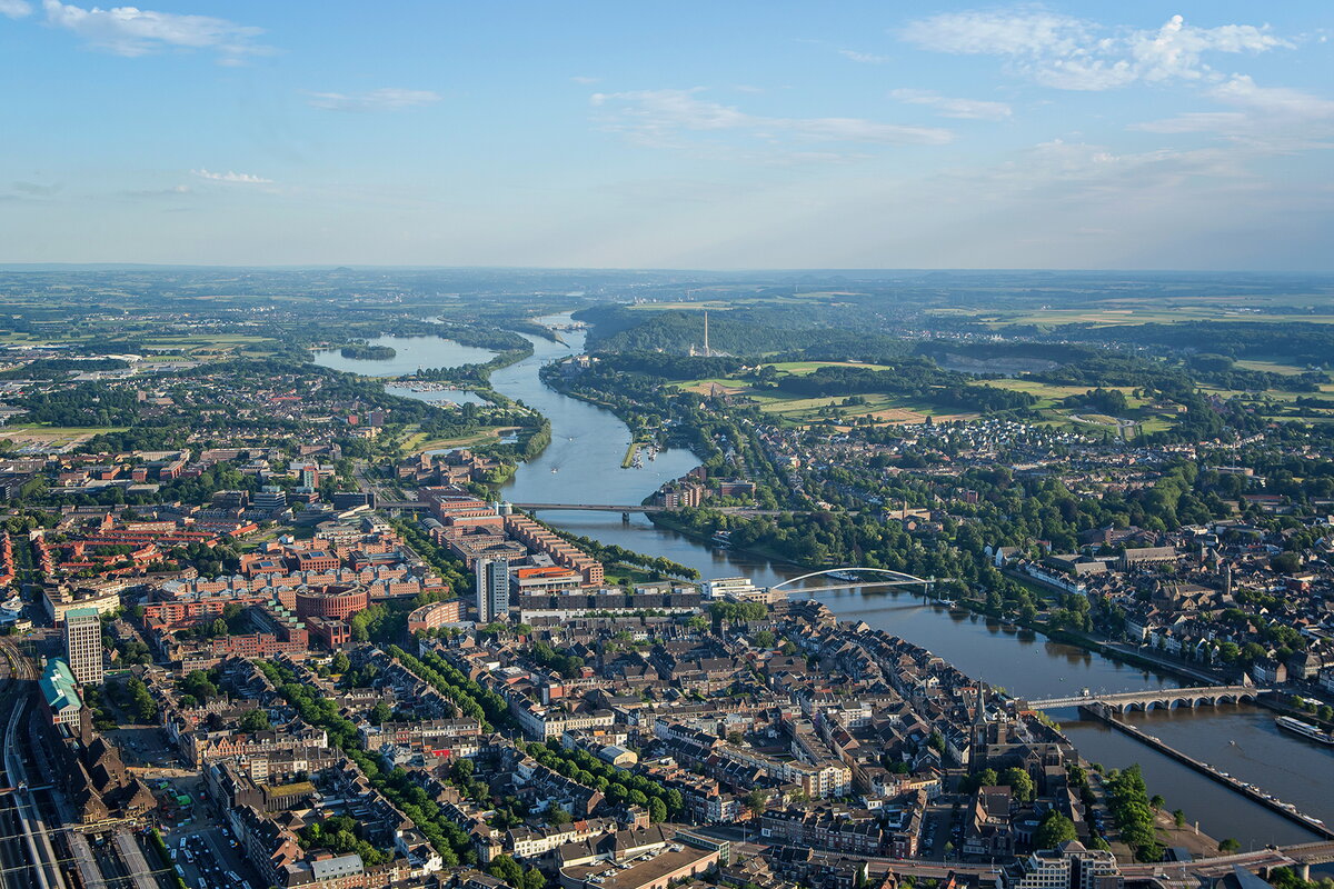 Aerial photo of Maastricht with the Meuse River flowing through the city. Houses are visible on both sides of the river. Three bridges cross the Meuse.