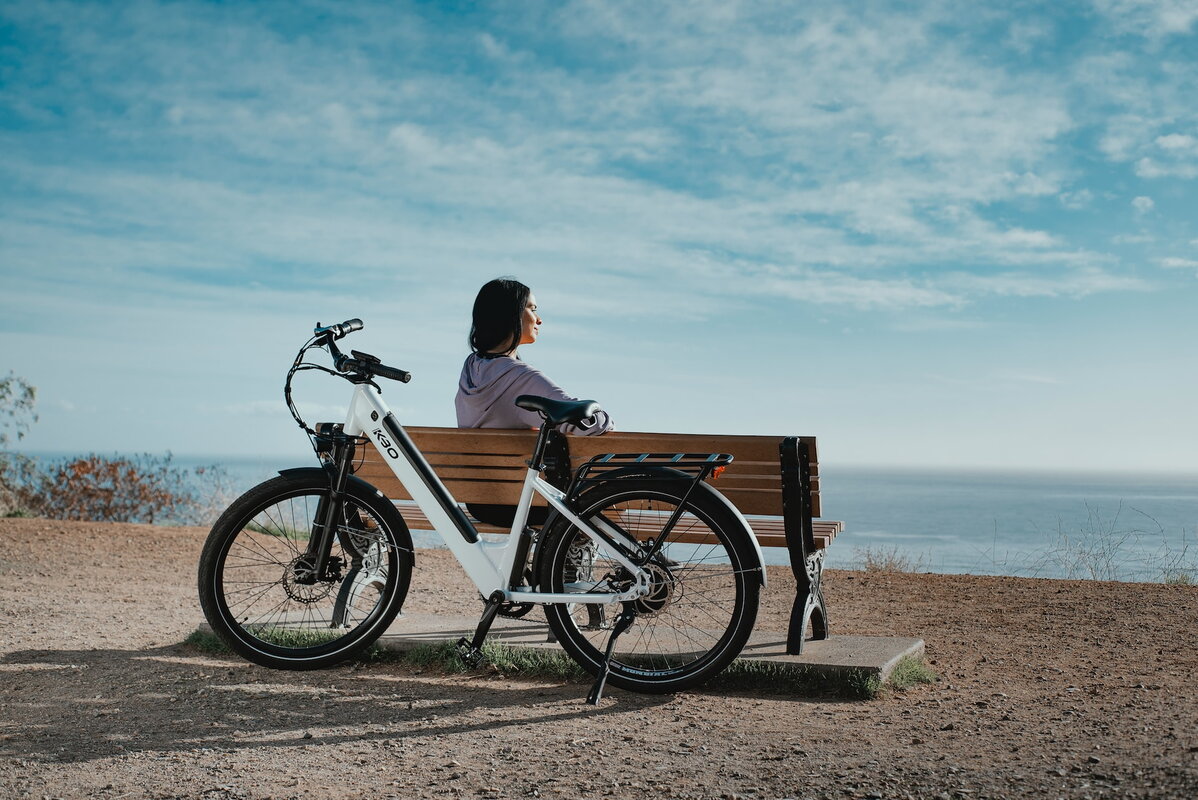 Mobilease vrouw zit op bankje en kijkt naar uitzicht fiets staat geparkeerd tegen bankje
