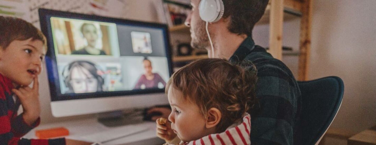 Vader werkt thuis aan bureau met koptelefoon op en twee kinderen aan het bureau