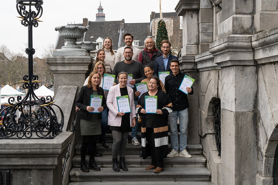 Deelnemers en trainers mobiliteitsmakelaars aan de training tot mobiliteitsmanagers op de examendag - Deelnemers staan op de trappen van het Stadhuis met hun certificaat in de handen