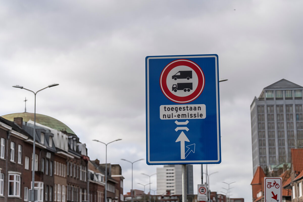 Blauw verkeersbord over zero-emissiezone tegen een grijze lucht en gebouwen