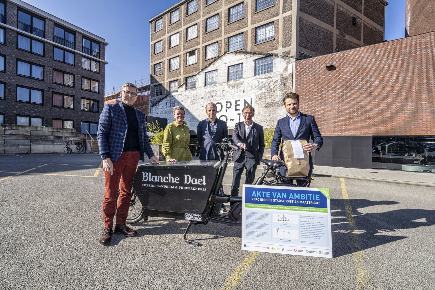 Employees from Blanche Dael and ZLB with an e-cargo bike and signed Declaration of Ambition. The photo shows two men from Blanche Dael and two male and one female employee from Zuid-Limburg Bereikbaar. The Declaration of Ambition is a large sign with the text “Declaration of Ambition” in a blue box. The cargo bike is black with a large Blanche Dael logo on the box. In the background, you can see the Blanche Dael building. The photo was taken in a parking lot.