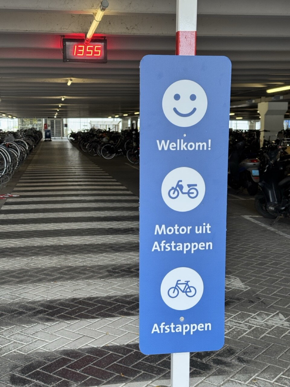 Blauw bord in fietsenstalling van het MUMC+ met daarop: Welkom - Motor uit afstappen - Afstappen