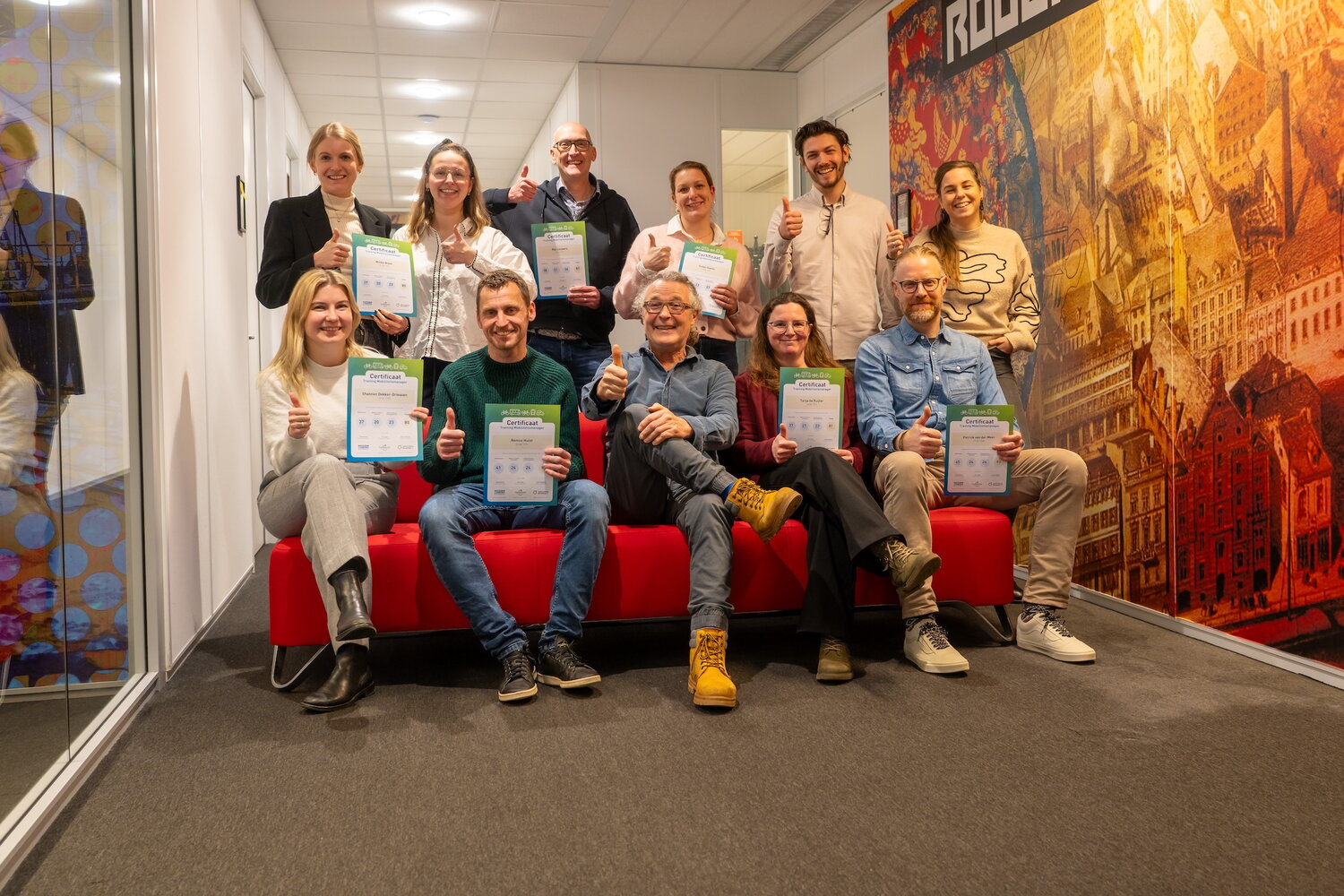 Groepsfoto examenkandidaten training Mobiliteitsmanager op 9 januari 2026 - 11 personen inclusief 4 trainers zitten op rode bank of staan achter de bank.